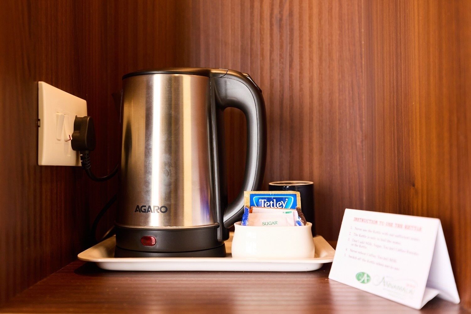 A stainless steel AGARO coffee maker on a white tray, a Tetley tea box, and a sign with instructions.