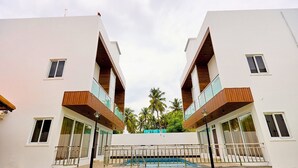 Un bâtiment moderne à deux étages, doté de balcons, d’une piscine et offrant une vue sur les palmiers.
