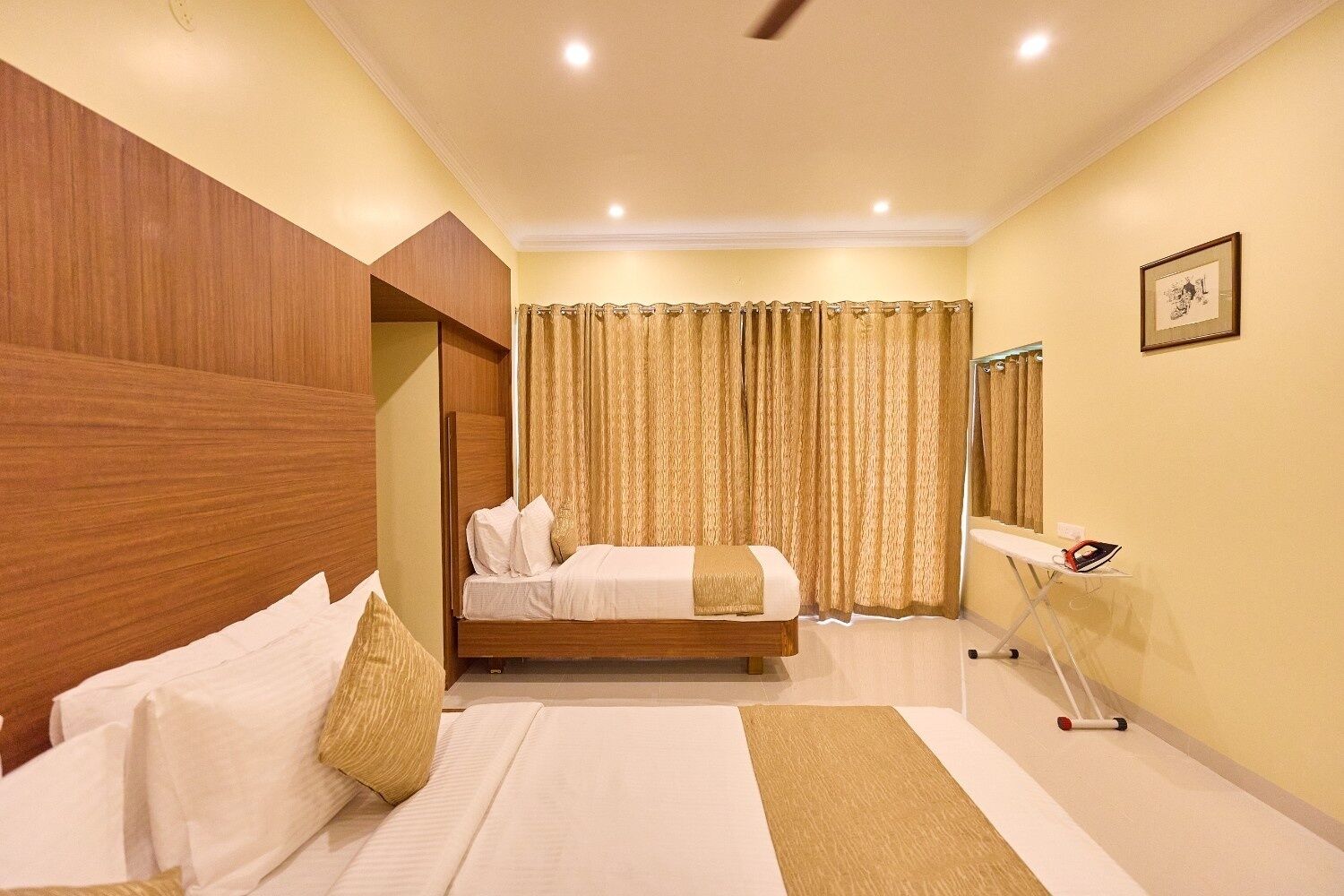A hotel room with a bed, a bedside table with an iron, a mirror, and a curtain.