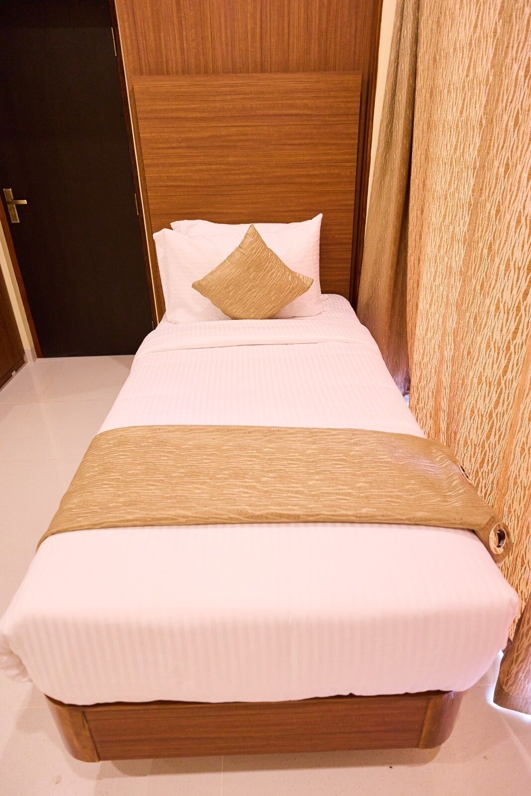 A neatly made bed with a wooden headboard, white bedding, and a decorative pillow.