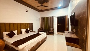 A bedroom with a large bed, a ceiling fan, a TV, and a door leading to a balcony. - Rajaji Retreat Resort (Ganga Bhogpur Talla)