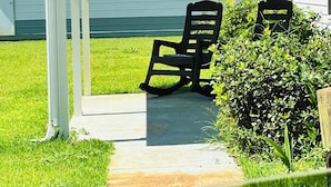 Ein überdachter Patio-Bereich mit zwei Schaukelstühlen, einer Rasenfläche und einem Gebäude im Hintergrund.
