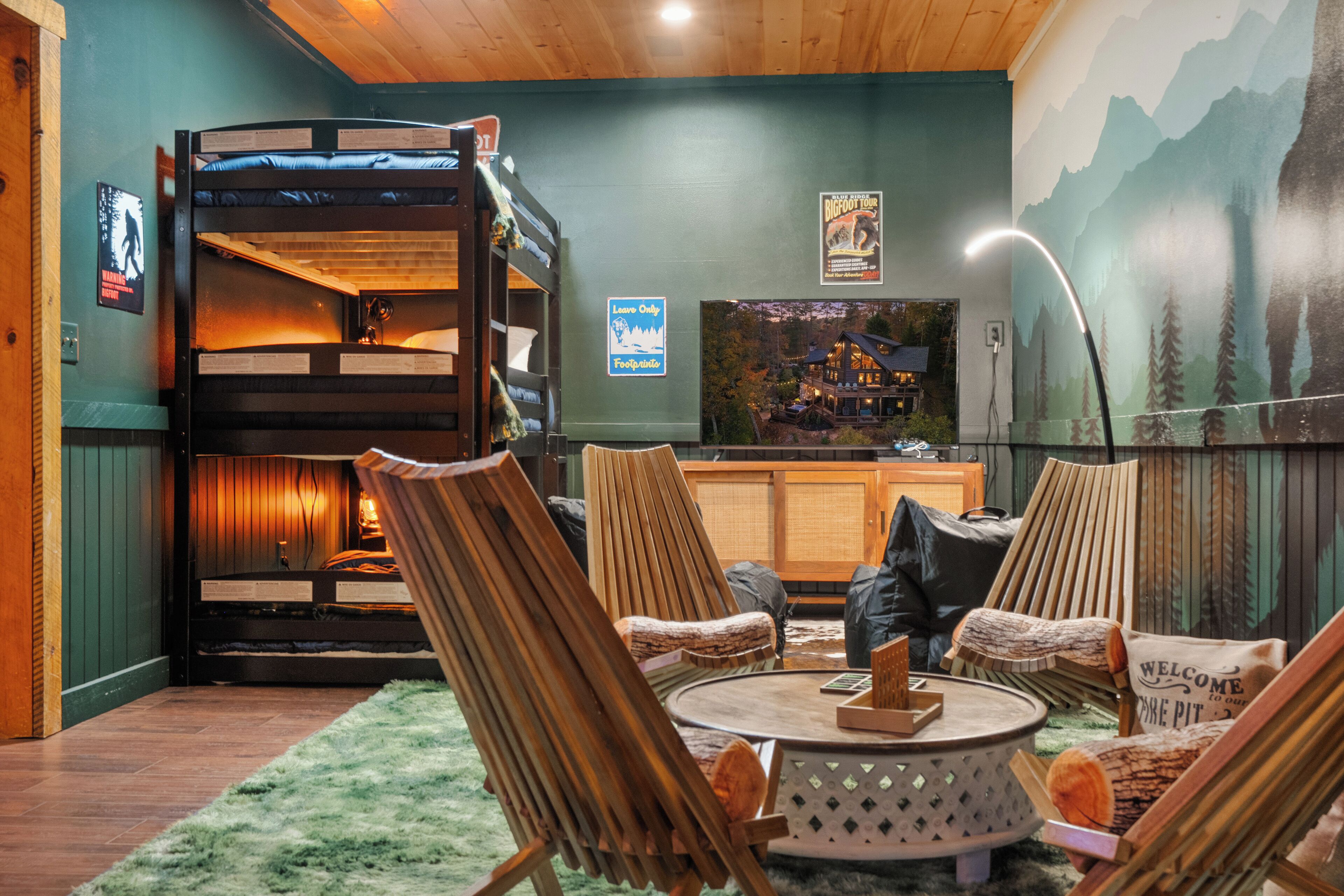 A cozy room with a bunk bed, wooden chairs, a round table, and a mural of mountains.