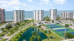 Un complejo hotelero de gran altura con varias construcciones, un patio central con piscina, canchas de tenis y vistas al océano.