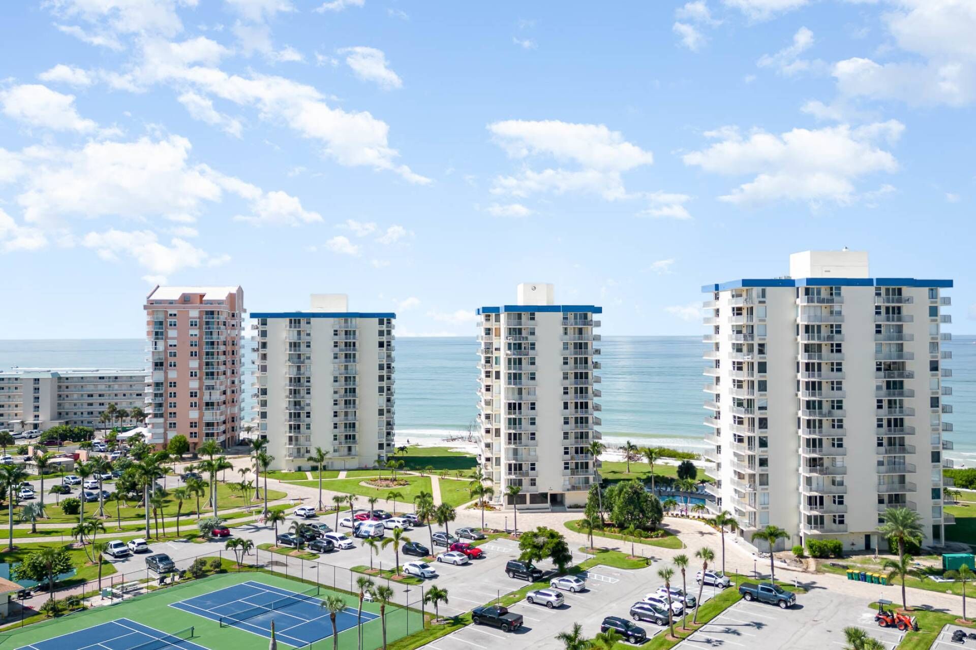 Un complejo hotelero frente a la playa con varios edificios de gran altura, un estacionamiento y una cancha de tenis.