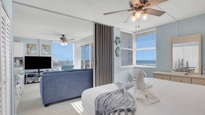 Un dormitorio con cama, ventilador de techo, televisor y vista al océano.