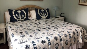 A bed with a nautical-themed bedspread, a wicker headboard, a bedside lamp, and a framed picture on the wall. - Family friendly 3-bedroom townhome with large sunroom  in St. Simons Island (St. Simons Island)