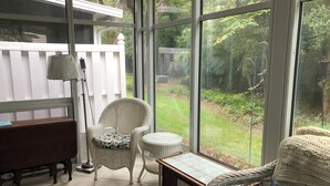 A conservatory with wicker furniture, a piano, and a view of a garden. - Family friendly 3-bedroom townhome with large sunroom  in St. Simons Island (St. Simons Island)