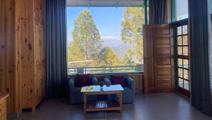 A wooden cabin interior with a large window, a sofa, and a small table. - Kasar Escape (Almora)