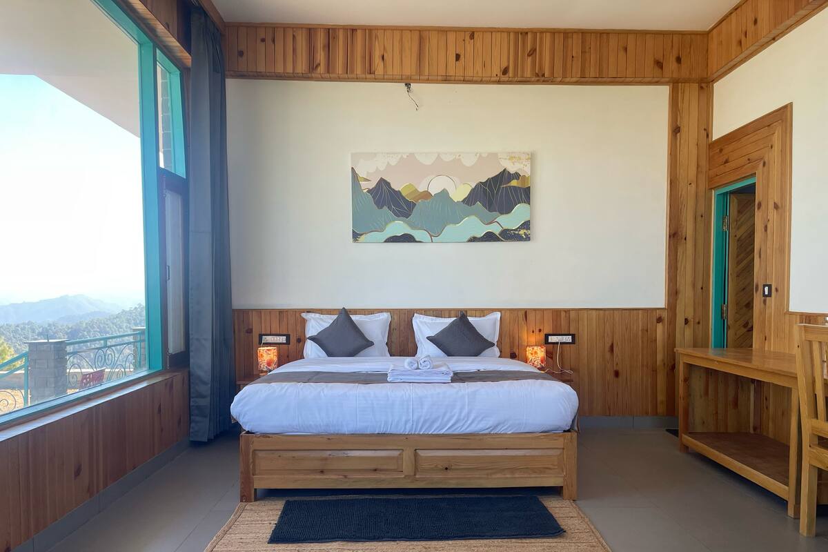 A wooden-paneled bedroom with a bed, a painting, and a view of mountains.