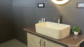 A bathroom with a beige sink, a round mirror with a light, a towel rack, and a small potted plant. - Kasar Escape (Almora)
