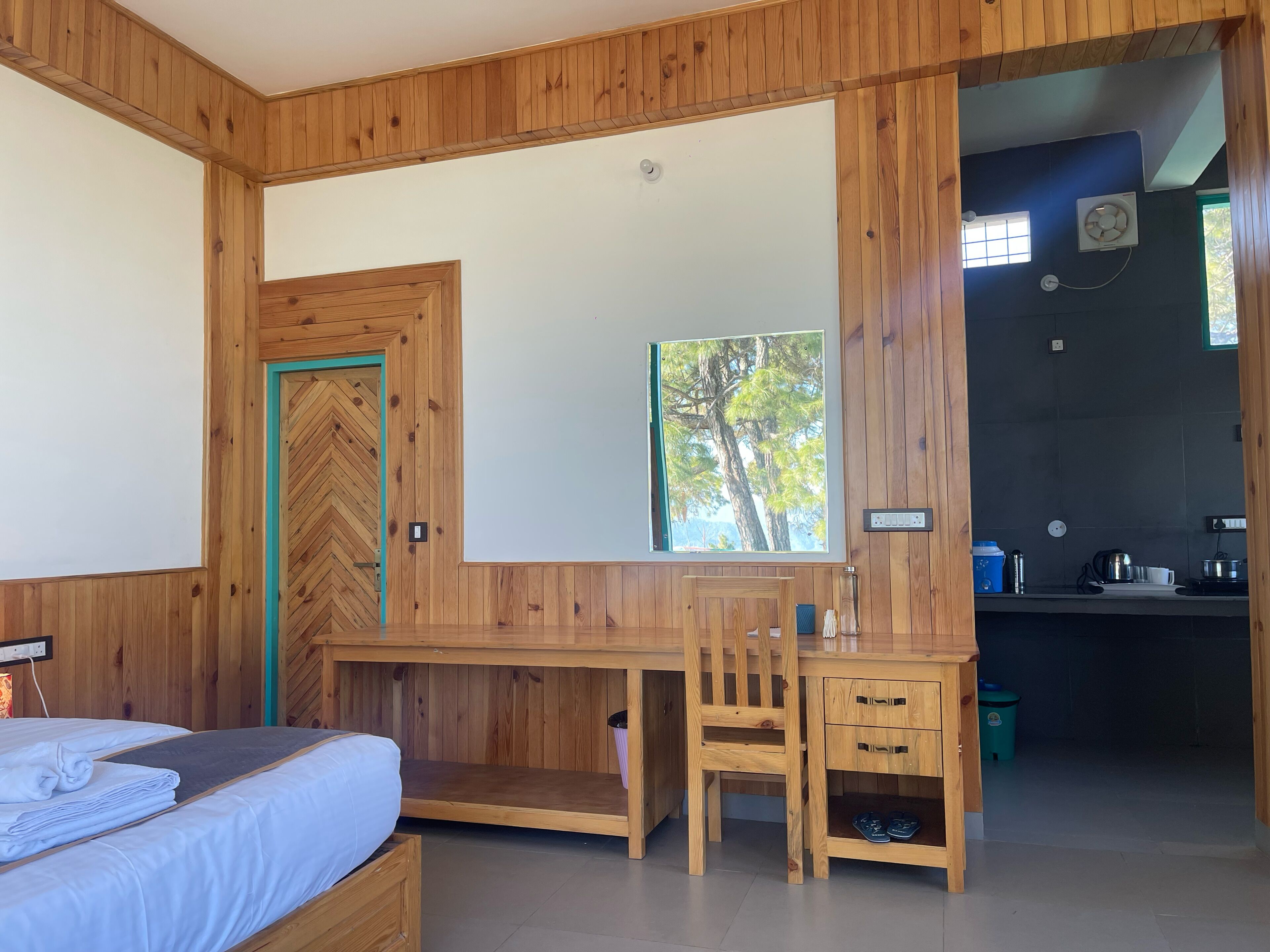 A wooden-paneled room with a bed, a desk, and a view of trees through a window.