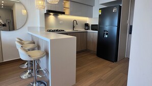 Een moderne keuken met een centraal eiland, barstoelen, een zwarte koelkast en hangende verlichting.