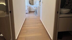 Een smalle gang met houten vloeren, witte muren en een spiegel aan de rechterkant.