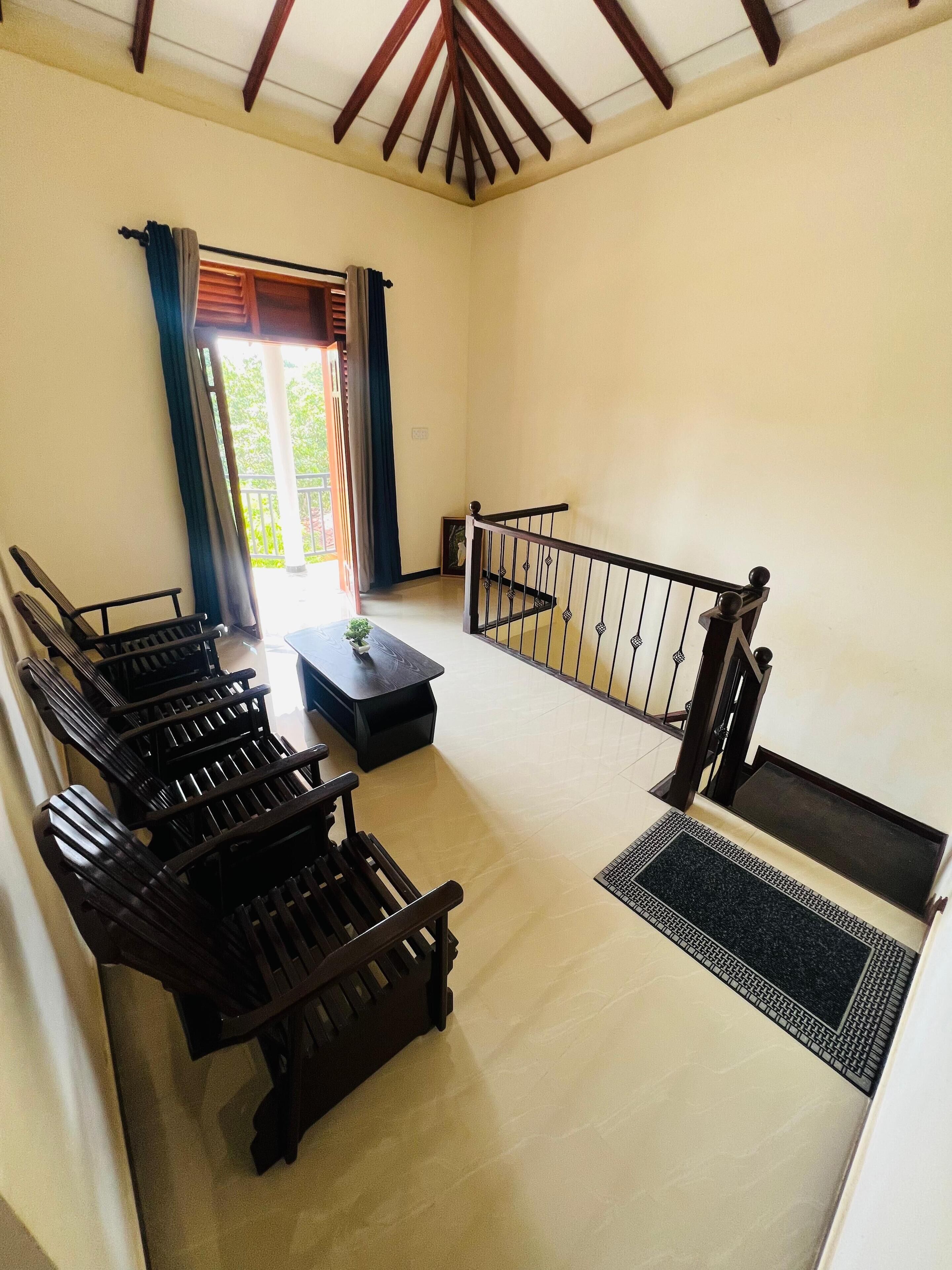 Un'ampia stanza con soffitto alto e un balcone. Diverse panche in legno sono disposte lungo le pareti, un tavolino con un vaso e un tappetino nero all'ingresso.