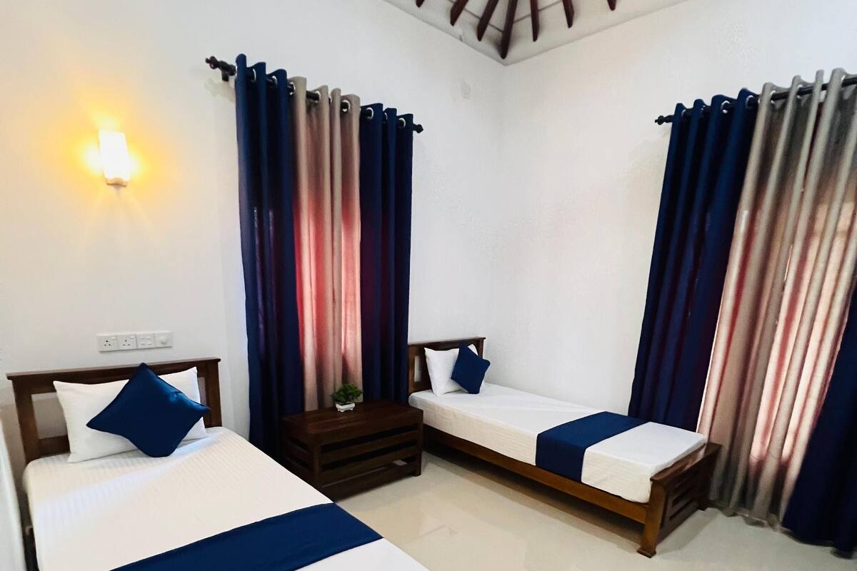 A hotel room with two beds, a nightstand, a wall-mounted light, and curtains.