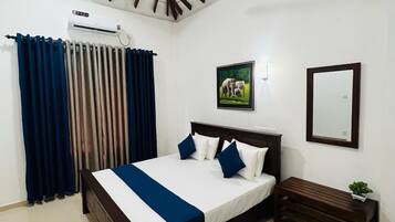 A bedroom with a bed, a ceiling fan, a window with curtains, a wall-mounted air conditioner, a framed picture, and a bedside table with a plant.