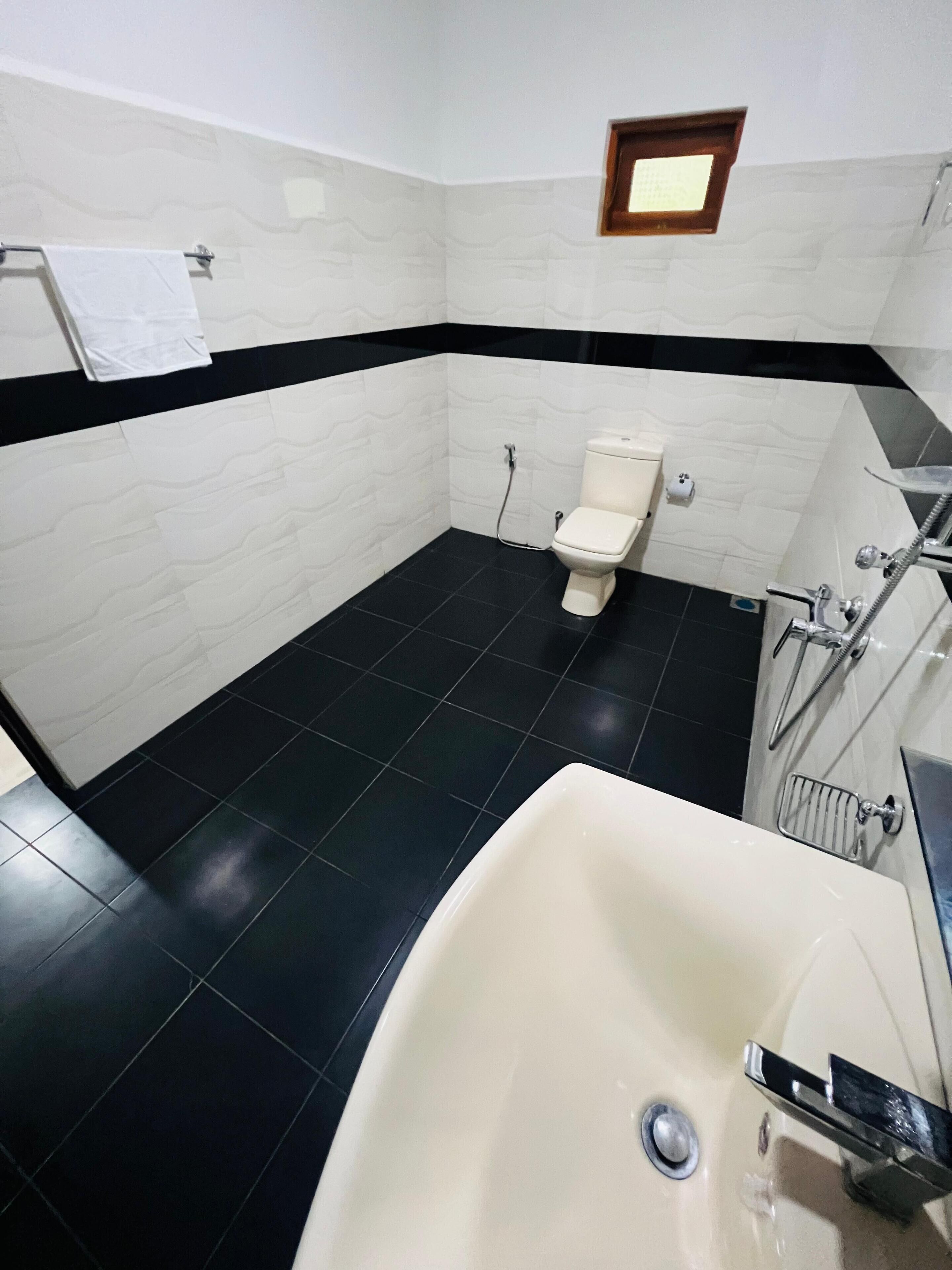 A bathroom with a white toilet, black tiled floor, and a white bathtub.