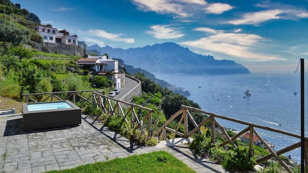 Une propriété située sur la côte, avec un chemin de pierre menant à une piscine, offrant une vue sur la mer et les montagnes.