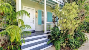 A porch with steps leading to a white door, surrounded by lush greenery. - Life Is A Breeze | Pool, Parking & Walk to Duval in Old Town Key West (Key West)