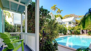 A poolside area with a covered porch, green chairs, and lush tropical vegetation. - Life Is A Breeze | Pool, Parking & Walk to Duval in Old Town Key West (Key West)