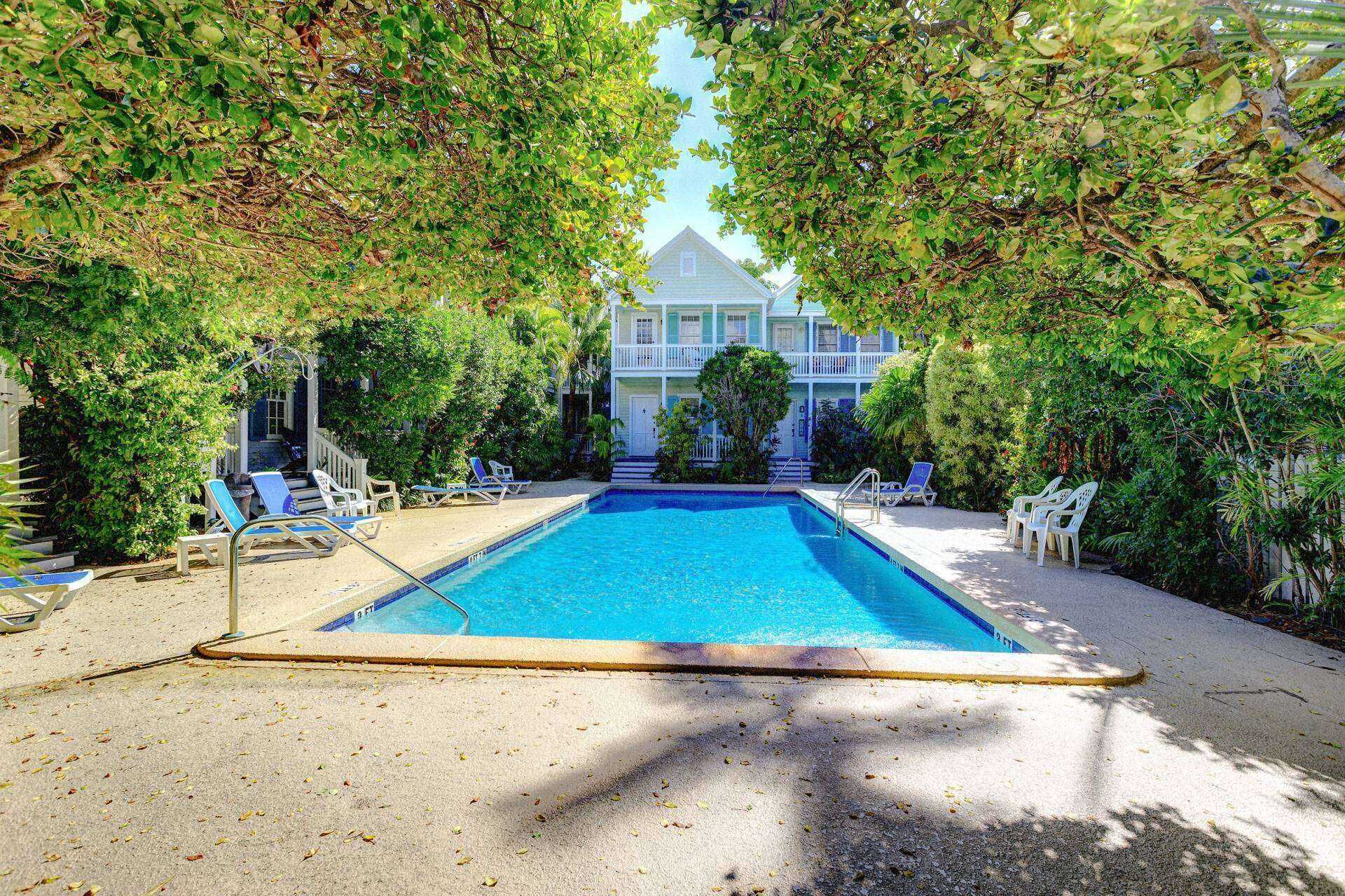 A swimming pool with lounge chairs, surrounded by dense foliage and a house in the background.