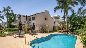 Ein Schwimmbecken mit gewölbter Kante, umgeben von einer Terrasse mit Gartenmöbeln.