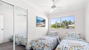 Ein Schlafzimmer mit zwei Betten, einem Deckenventilator, Blick auf den Strand und einer Tür, die auf einen Balkon führt.
