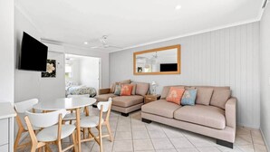 Ein modernes Wohnzimmer mit einem beigefarbenen Sofa, einem Esstisch mit Stühlen und einem großen Spiegel an der Wand.