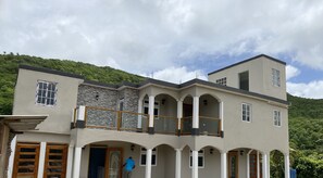 Un edificio de varios pisos con un balcón, ventanas arqueadas y montañas al fondo.