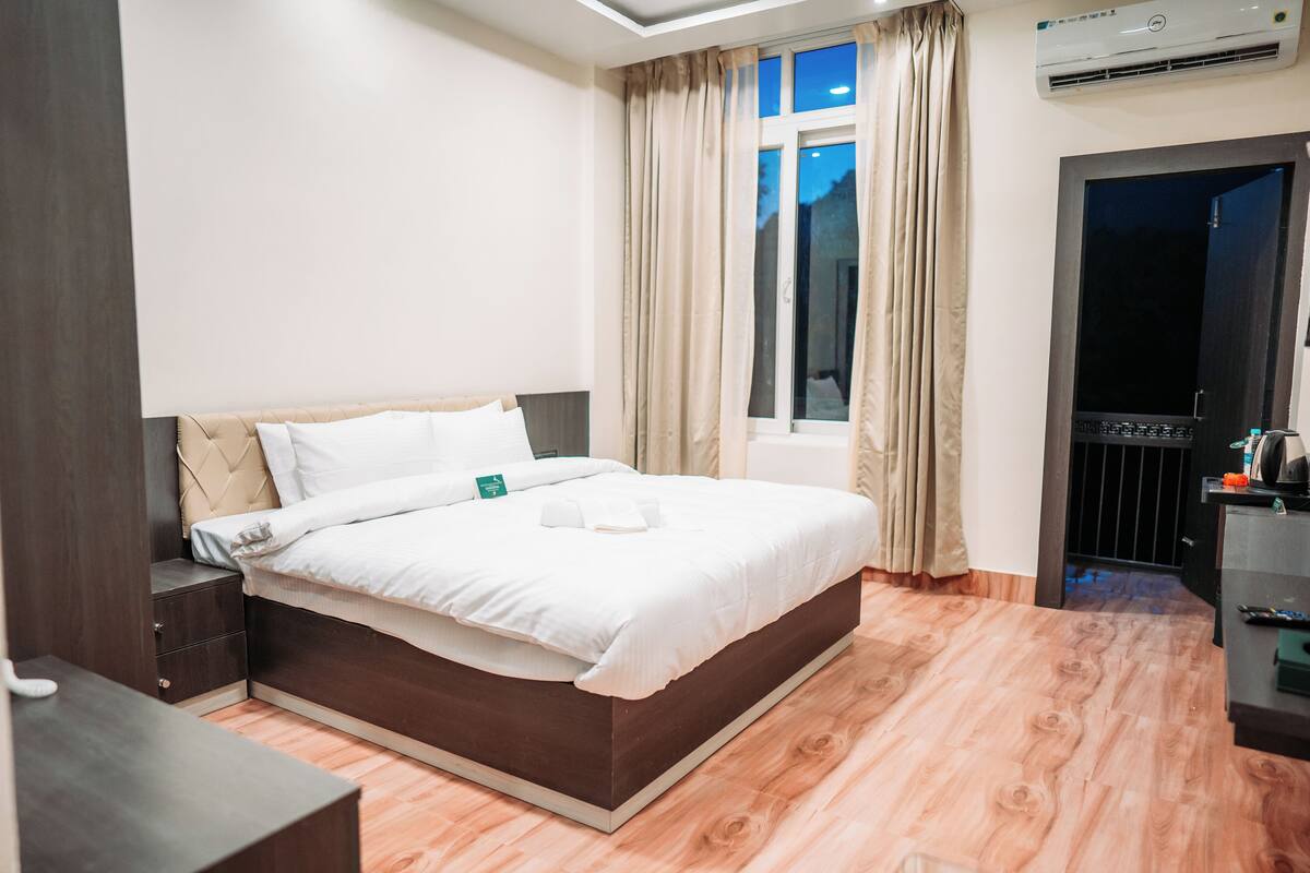 A hotel room with a large bed, a bedside table, a wardrobe, and a window with curtains.