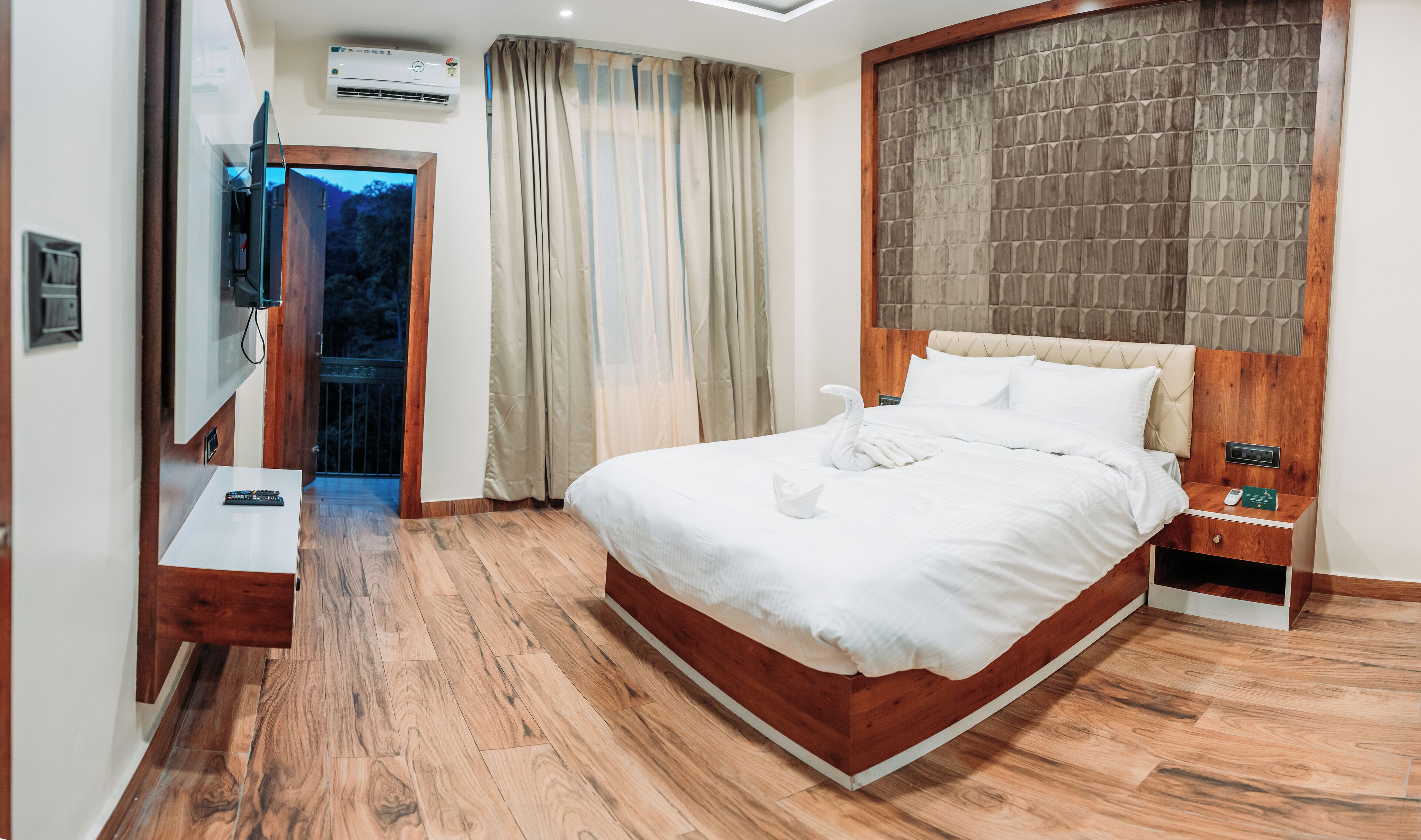A modern hotel room with a wooden bed, a flat-screen TV, and a wooden floor.