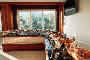 A buffet setup with multiple serving stations and a view of the outdoors through large windows.