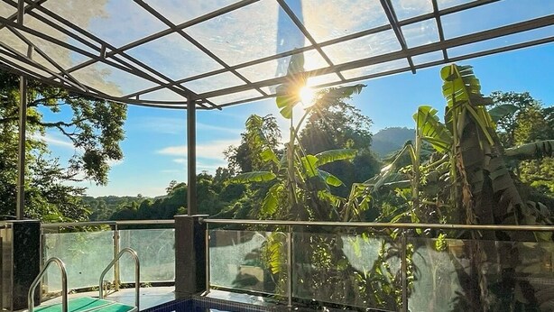An indoor swimming pool with a glass ceiling, surrounded by tropical plants and a view of the sky. - Papumpare Jungle Resort (Papumpare)