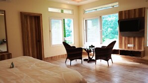 A hotel room with a bed, two chairs, a table, a TV, and large windows. - Papumpare Jungle Resort (Papumpare)