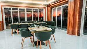 A modern dining area with a large table and chairs, large windows with a view, and a wooden accent wall. - Papumpare Jungle Resort (Papumpare)