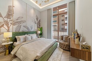 Une chambre d’hôtel moderne avec un grand lit, une tête de lit verte, une table de chevet en bois, un fauteuil vert et une vue sur la façade de l’immeuble par une grande fenêtre.