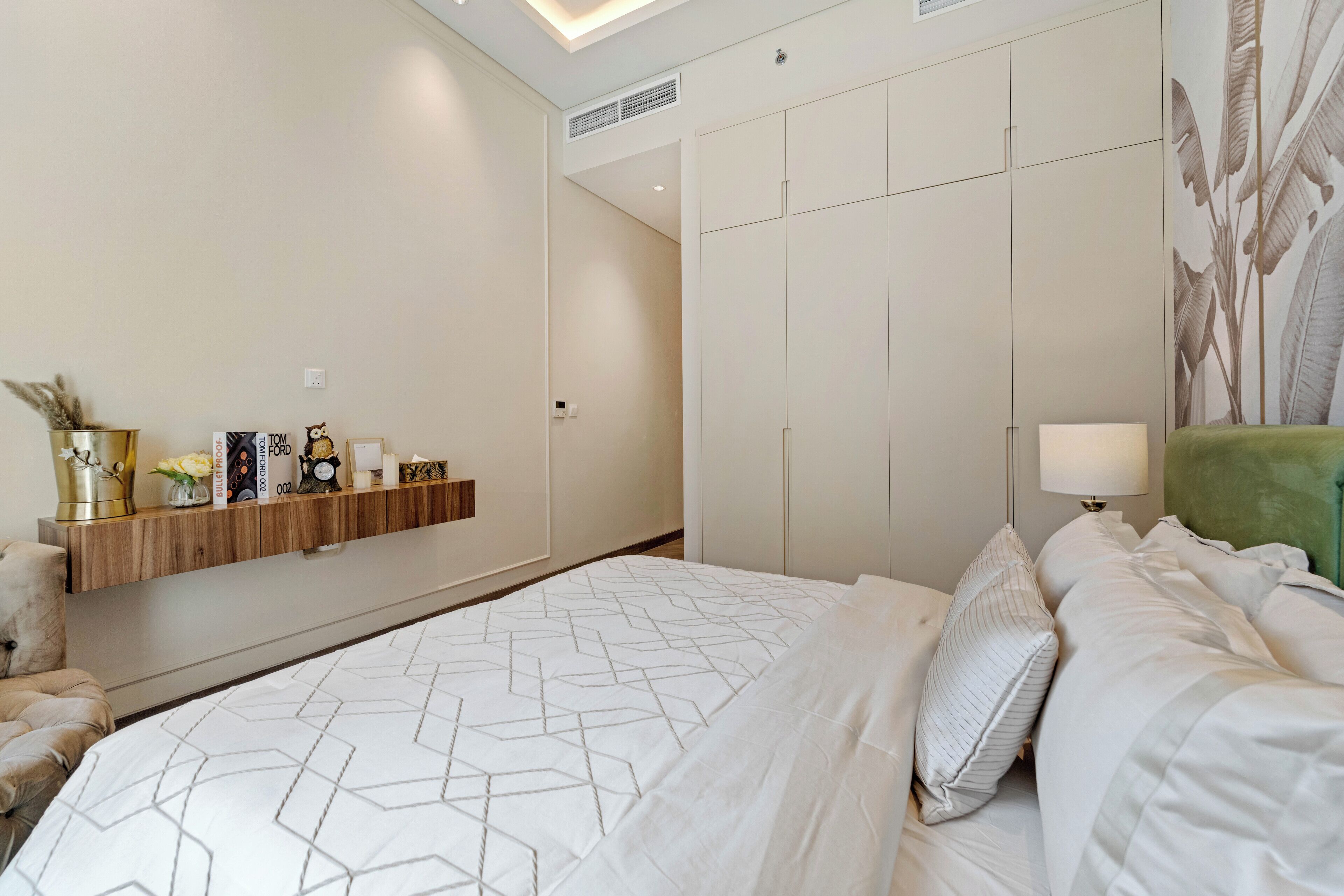 Een moderne hotelkamer met een groot bed, een nachtkastje, een wandplank met decoratieve objecten, en een groot raam met uitzicht.