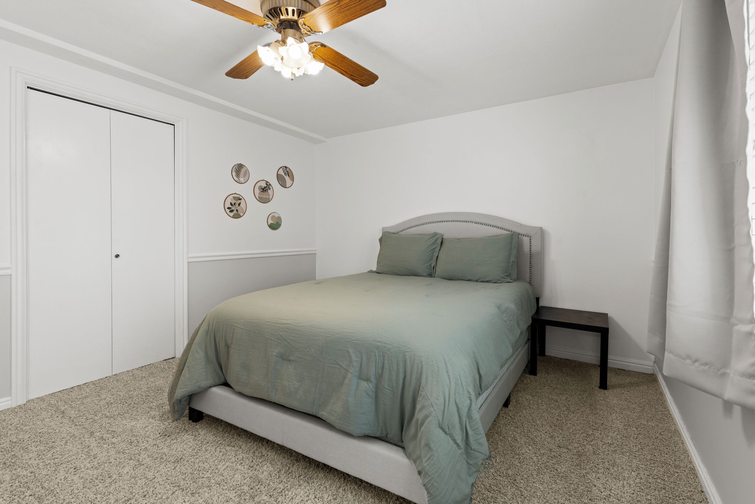 A bedroom with a bed, a ceiling fan, a small bedside table, and a door.