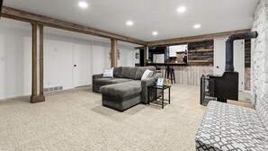 A spacious living area with a grey sectional sofa, a patterned sofa, and a small coffee table. The room features exposed wooden beams, a white door, and a kitchen area in the background. - East Farmington Hideaway (Farmington)