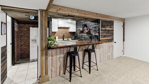 A kitchen with a wooden bar counter, two bar stools, a coffee machine, and a brick wall. - East Farmington Hideaway (Farmington)