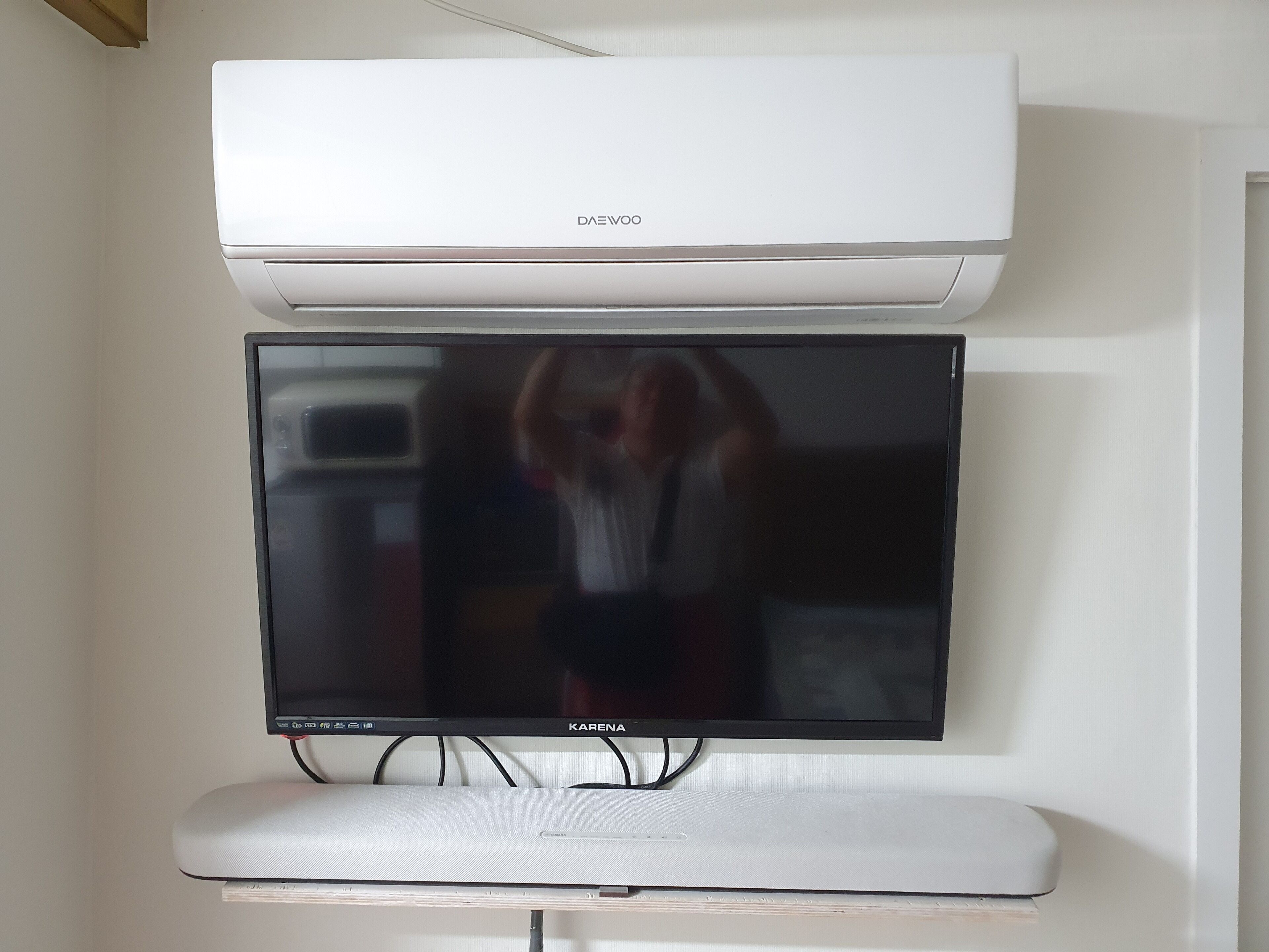 A flat-screen TV mounted on a wall, with a white air conditioning unit above it.