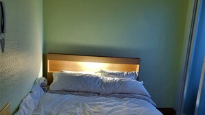 A bed with a wooden headboard, white bedding, and a window to the right.