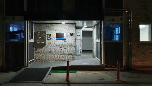 An entrance to a building with a brick wall, a door, and a ramp leading inside.