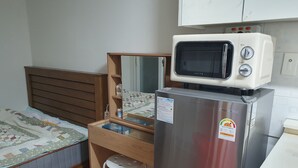 A compact kitchenette with a microwave, refrigerator, and wooden desk.