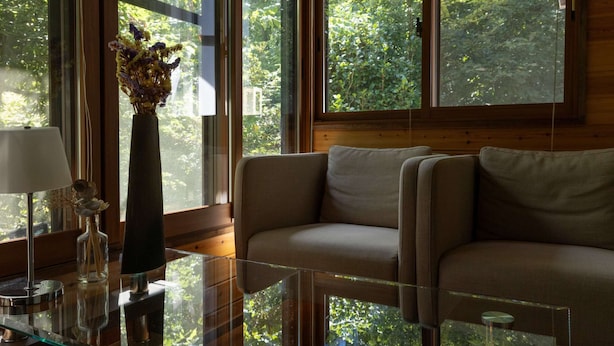 Una sala de estar moderna con una mesa de centro de vidrio, un sofá color beige y un jarrón con flores secas.