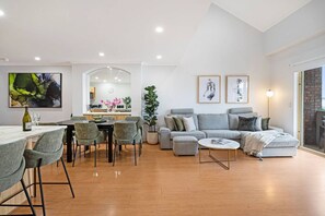 A modern living room with a grey sofa, a dining area with a table and chairs, and a kitchen in the background. - Adelaide `Hills-View` Retreat (Adelaide)