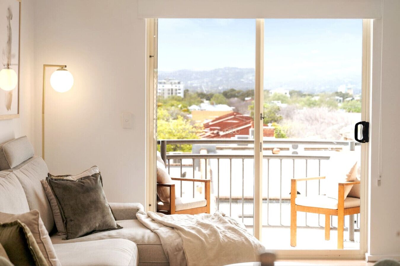 Ein Wohnzimmer mit einer Couch, zwei Sesseln und Blick durch eine Schiebetür auf einen Balkon.