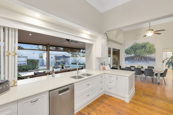 A modern kitchen with a large island, built-in appliances, and a dining area with a view of the backyard. - The Retreat on Chaffey (Mildura)