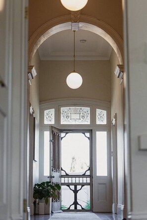 A hallway with an arched ceiling, a hanging light fixture, and a decorative door with a window. - The Retreat on Chaffey (Mildura)